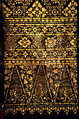 Wat Xieng Thong temple in Luang Prabang, Laos. Detail of the  intricate gold stencilling on black lacquer that decorate the walls of the sim. Floral motif.